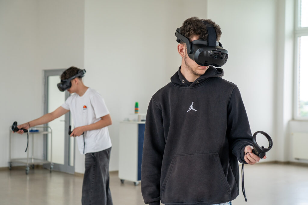 Schüler tragen Virtual Reality Headsets und strecken ihre Arme mit Controlern aus